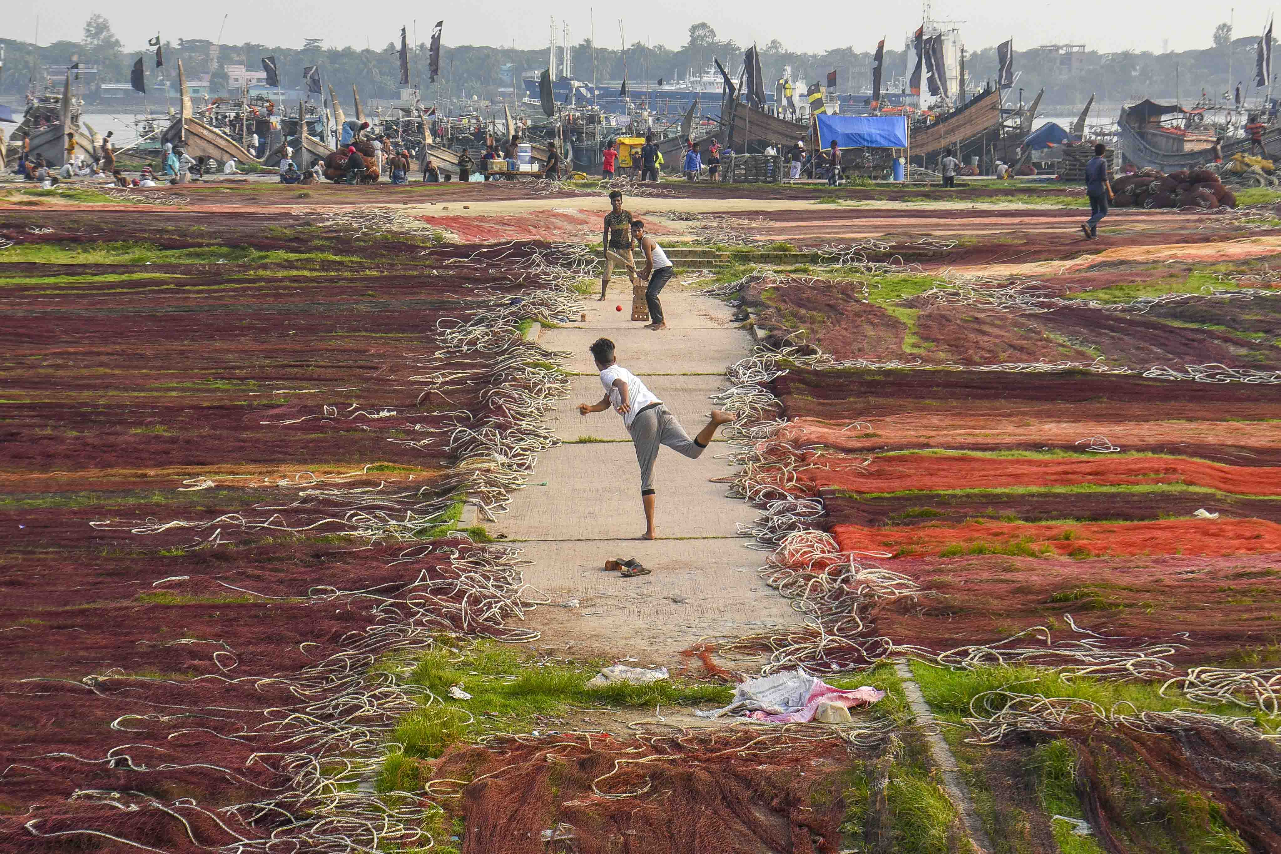 Three youths play a game of cricket in one of the few spots in a field not covered by drying fishing nets at Fishery Ghat.