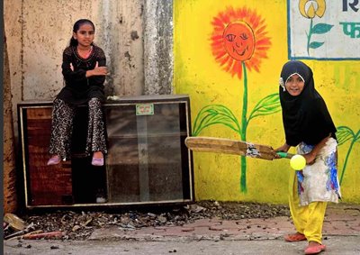 a Mumbai girl plays street cricket whilst her friend waits her turn to bat.